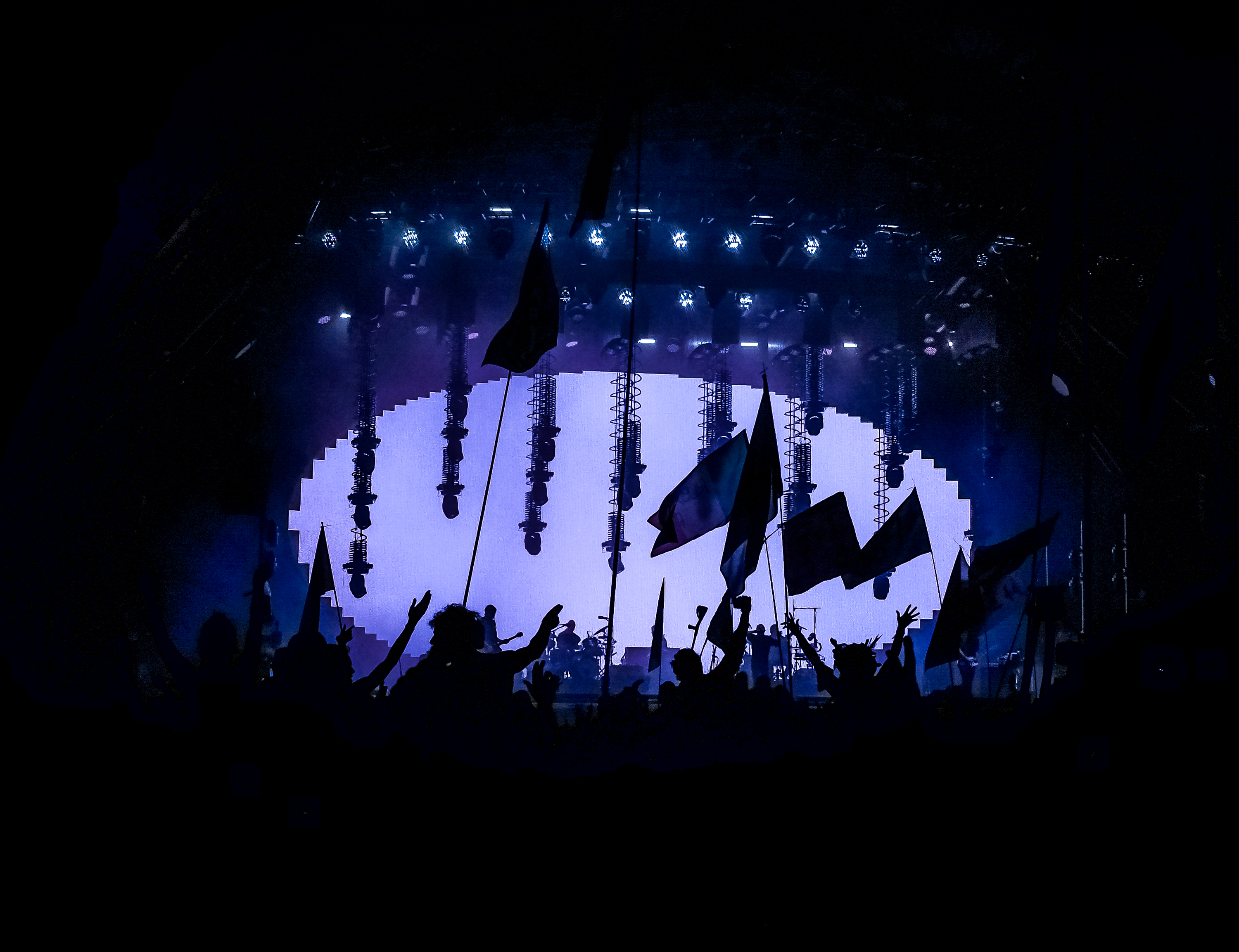 Silhouette del pubblico con bandiere davanti allo schermo ovale illuminato di viola durante il concerto dei Radiohead a Glastonbury 2017