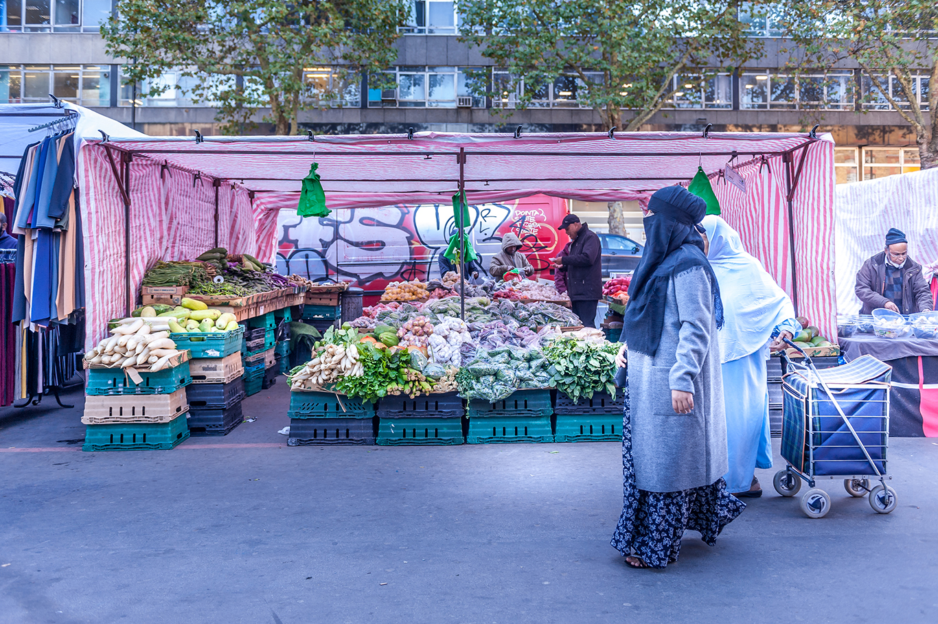 Passanti davanti a un banco di frutta e verdura in un mercato di strada dell'East London, Londra