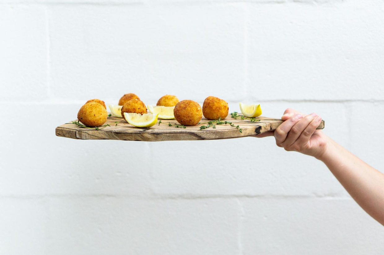 person holding chopping board with meatballs and sliced lemons