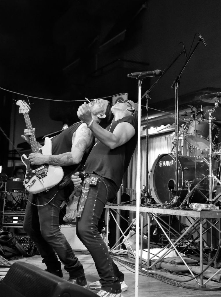 Due musicisti si esibiscono in un concerto dal vivo, immersi nella musica, uno con una chitarra e l'altro che canta, in un intenso momento di connessione.