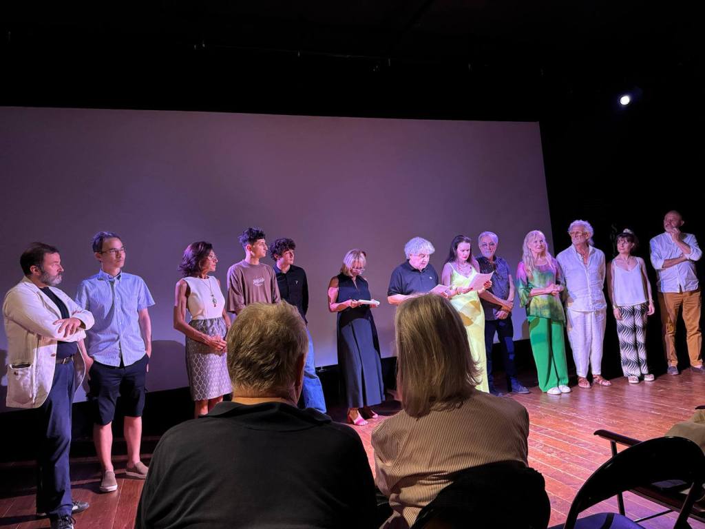 Un gruppo di persone sul palco durante una cerimonia di premiazione, con un grande schermo sullo sfondo.