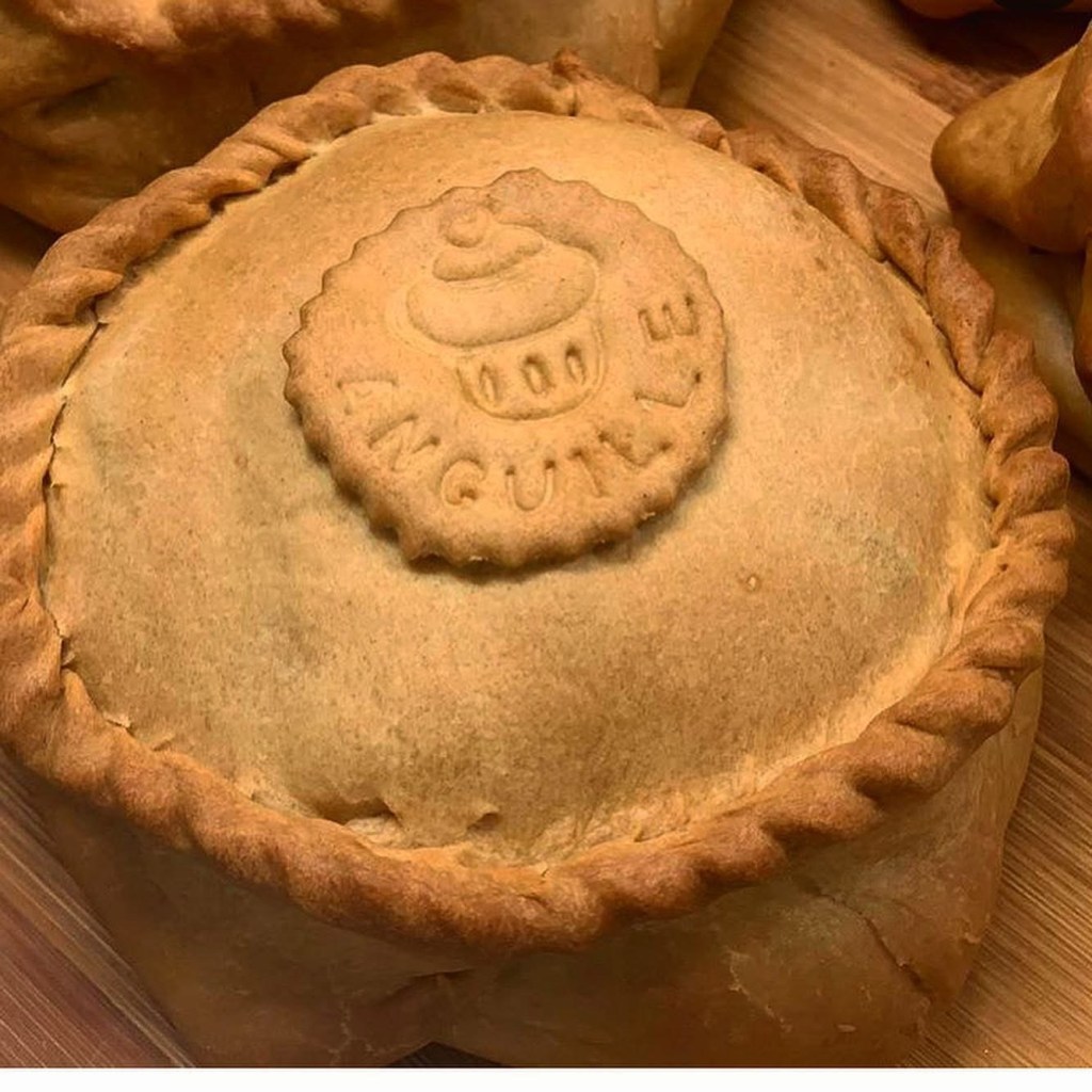 Un primo piano di una panada, un pasticcino tradizionale sardo, con un coperchio dorato e una decorazione stampata al centro, su un fondo di legno.