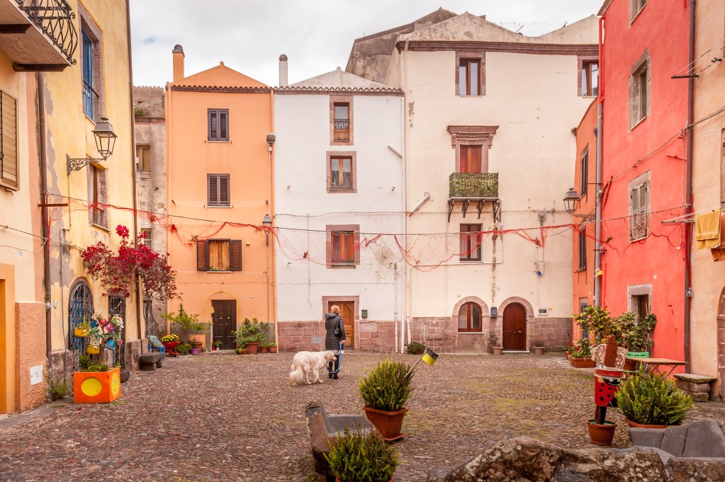Piccola piazza acciottolata nel centro storico di Bosa, Sardegna, con case colorate, insegne artigianali e atmosfera autentica mediterranea