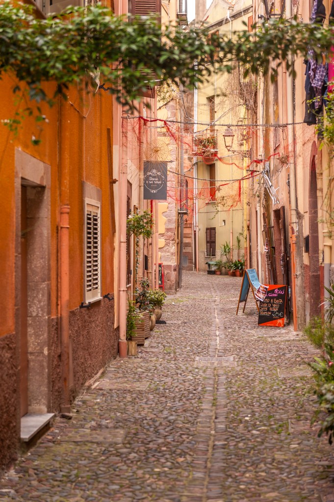 Stretta via acciottolata nel centro storico di Bosa, Sardegna, con case colorate, insegne artigianali e atmosfera autentica mediterranea