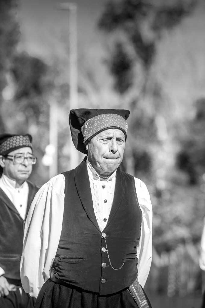 Uomo in costume tradizionale sardo durante la Sagra de Sa Panada, con un'espressione seria e sfondo sfocato.