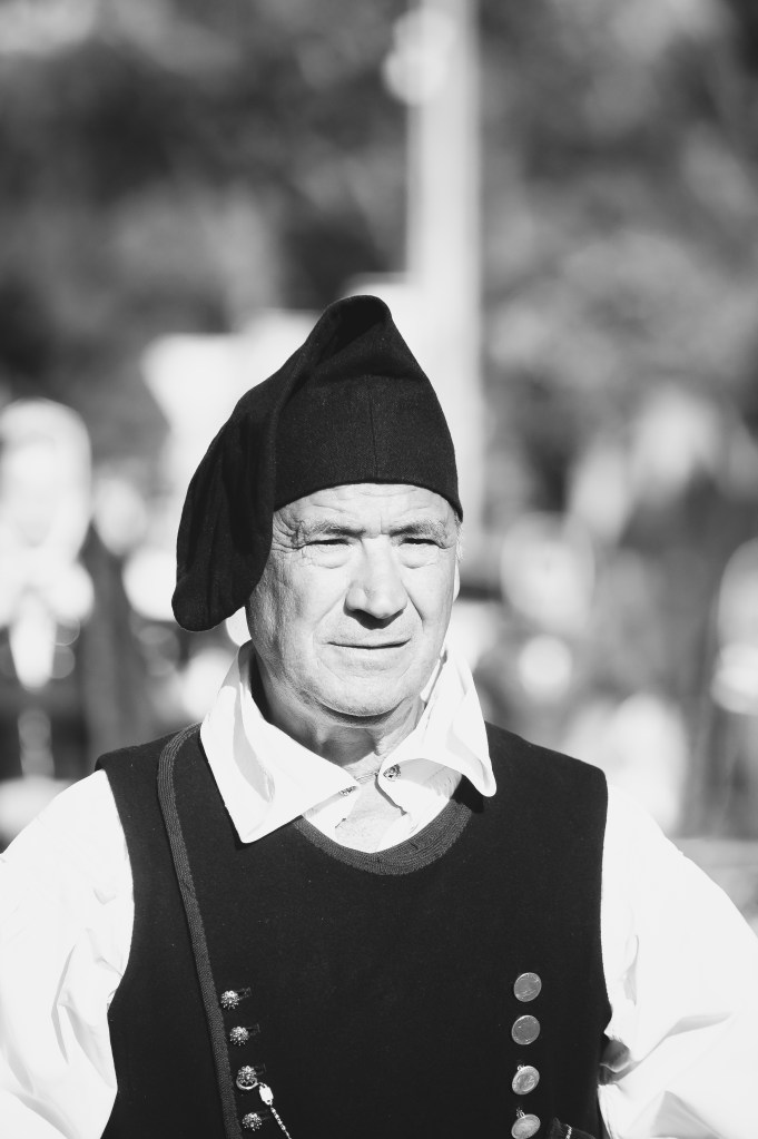 Ritratto in bianco e nero di un uomo in costume tradizionale sardo durante la Sagra de Sa Panada, con un'espressione seria e fiera.