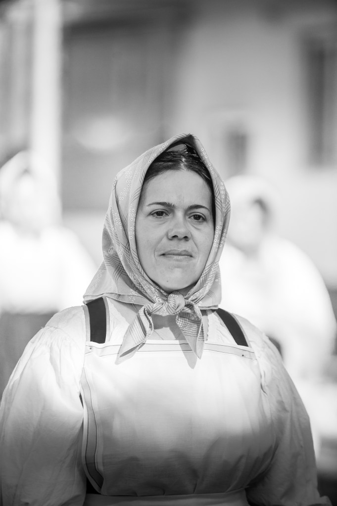 Ritratto in bianco e nero di una donna in costume tradizionale sardo, con un fazzoletto in testa e un'espressione serena, durante la Sagra de Sa Panada ad Assemini.