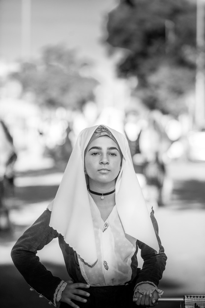 Giovane donna in costume tradizionale sardo durante la sfilata folkloristica della Sagra de Sa Panada 2025 ad Assemini. Ritratto in bianco e nero che cattura fierezza ed eleganza.