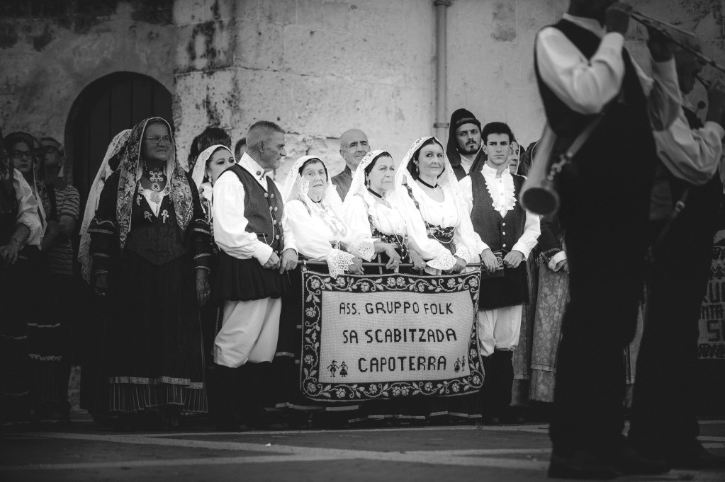 Gruppo folkloristico in costumi tradizionali sardi durante la Sagra de Sa Panada, con un'insegna che recita 'ASS. GRUPPO FOLK SA SCABITZADA CAPOTERRA'.