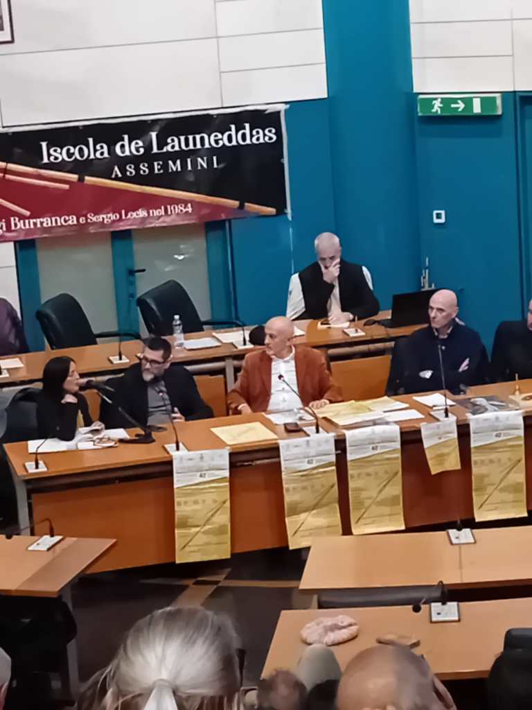 Un panel di relatori durante l'evento 'Launeddas in Comune' ad Assemini, con documenti e materiali informativi sul tavolo.