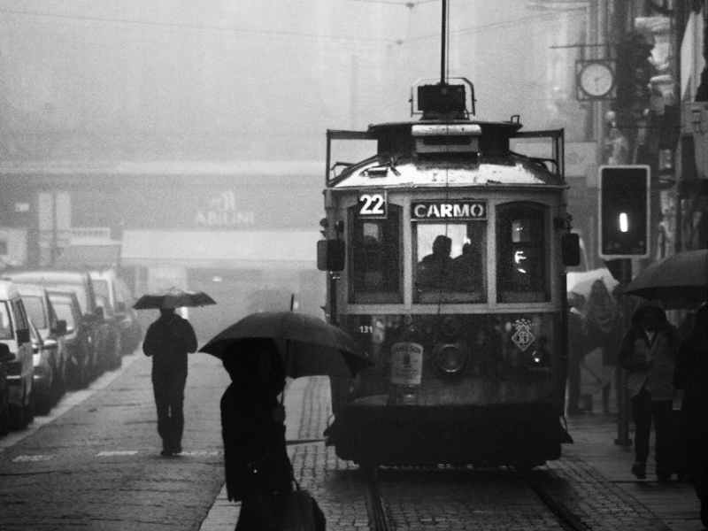 grayscale photography of person crossing street near a tram