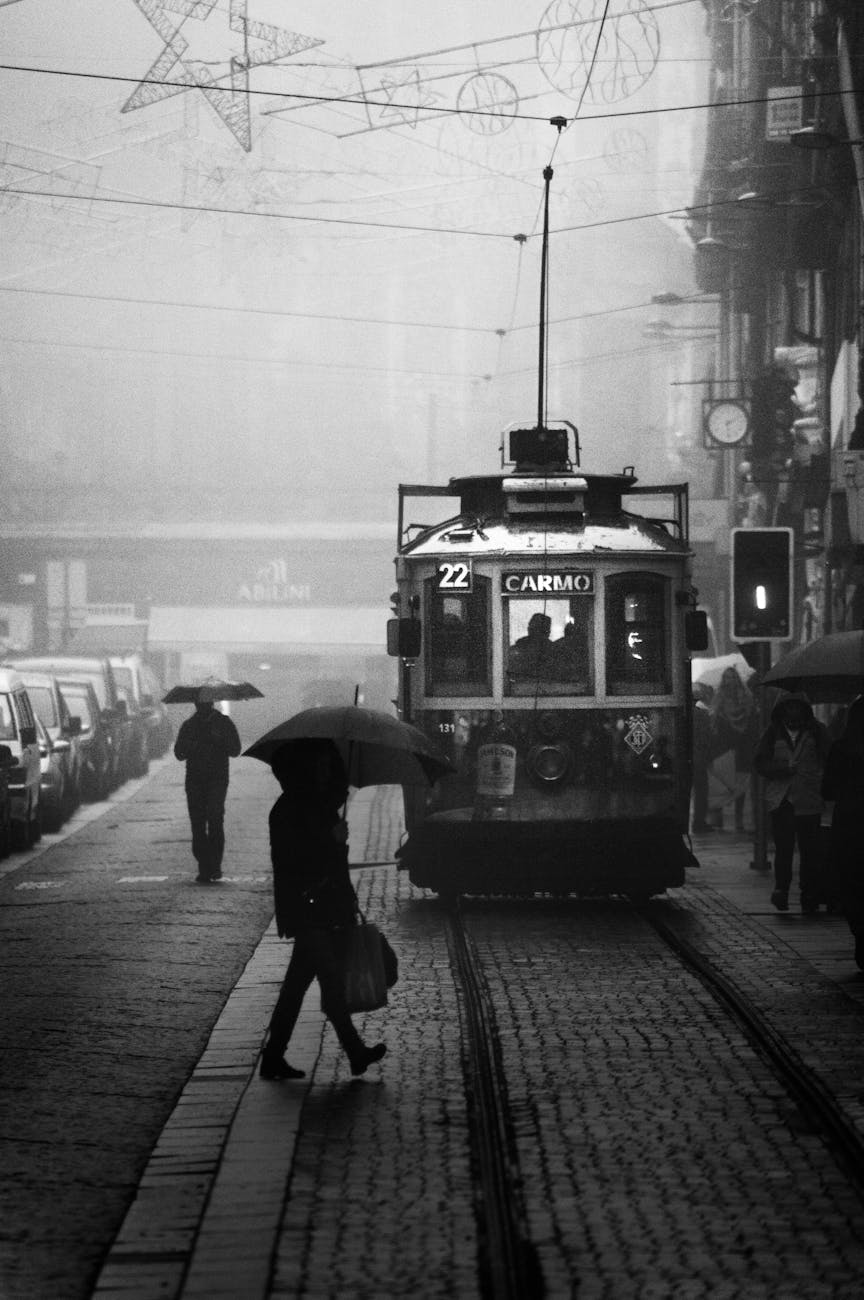 grayscale photography of person crossing street near a tram