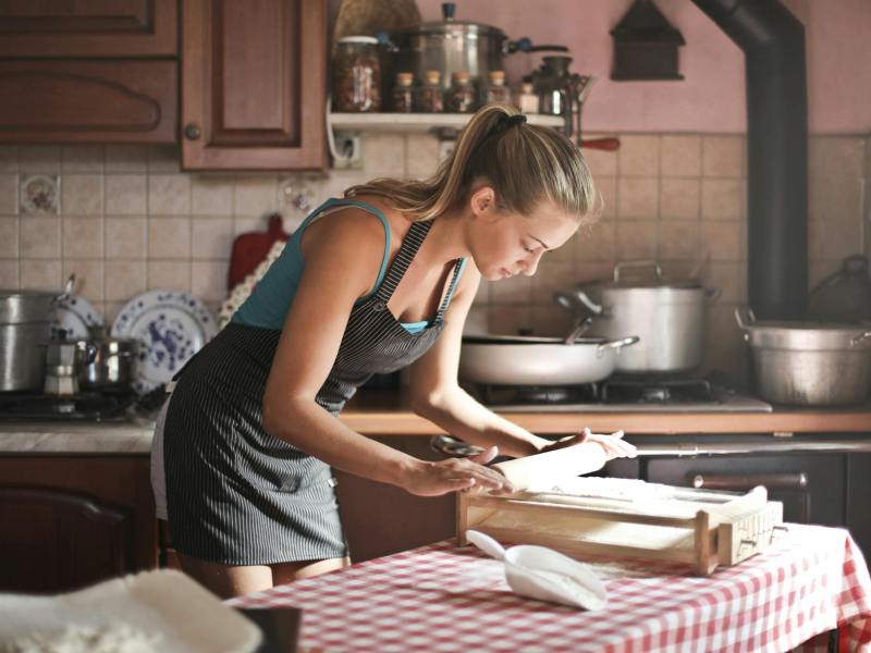 young woman rolling dough for baking in kitchen