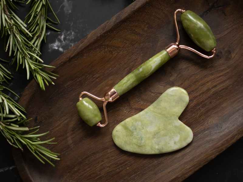 set of facial massage tools placed on wooden plate on black table