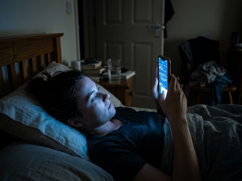 Woman lying in bed looking at smartphone in dark room